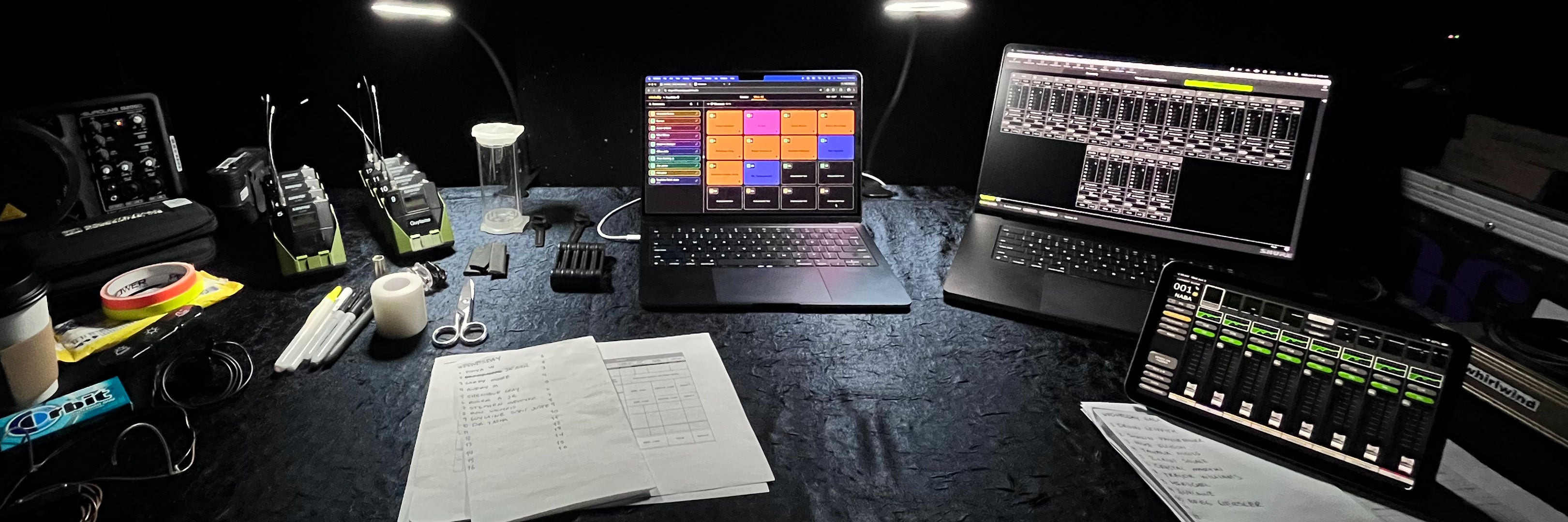 micAddy open on a laptop at a live event tech table, beside wireless bodypacks in StageStrike packHolders, a mixing console, and a printed run-of-show.